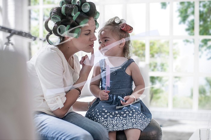 Mother in hair rollers pointing cheek to daughter