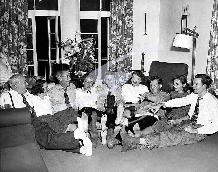 United States: 1954 Nine barefoot adults sitting on the floor with their feet in the middle.. Barefoot Adults Laughing