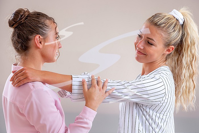 Complicity - young women face to face on a light gray background