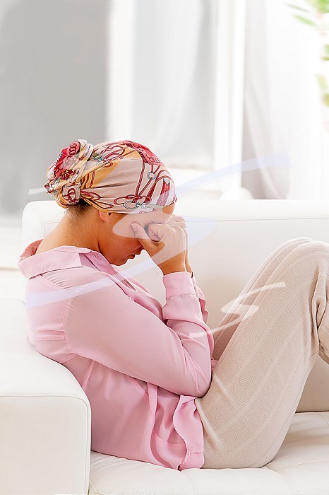 Woman wearing a headscarf, in profile, curled up on the sofa, her fists clenched against her eyes.