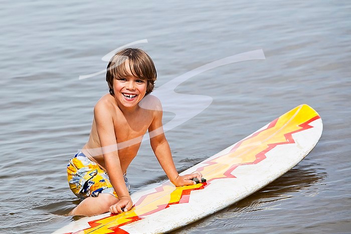 Young happy boy playing in water on a surfboard.  Lake Winnipeg, Gimli, Manitoba, Canada.