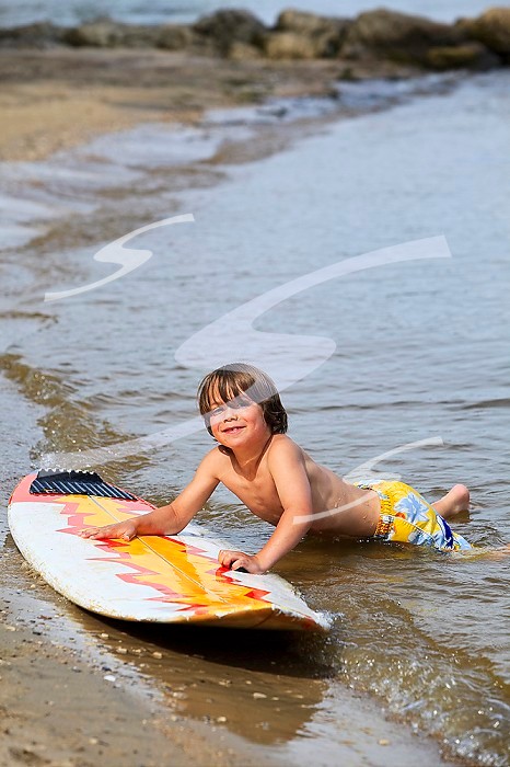 Young smiling boy playing with surfboard on Lake Winnipeg.  Gimli, Manitoba, Canada.