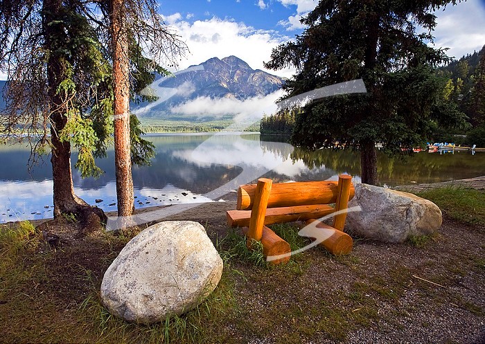 Middle age male sitting on bench at Pyramid Lake looking at Pyramid Mountain, Jasper National Park, Alberta, Canada.